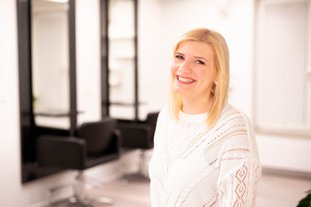 A person in a white lace dress poses in a bright modern interior space with black framed artwork.