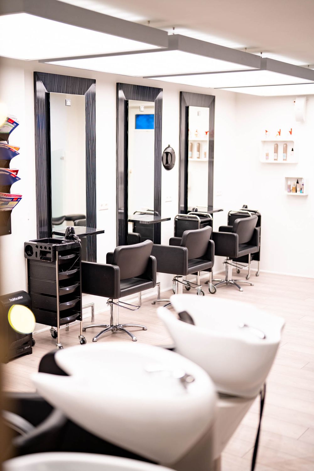 Modern hair salon interior with black styling chairs, white shampoo stations, and bright lighting in a minimalist space.