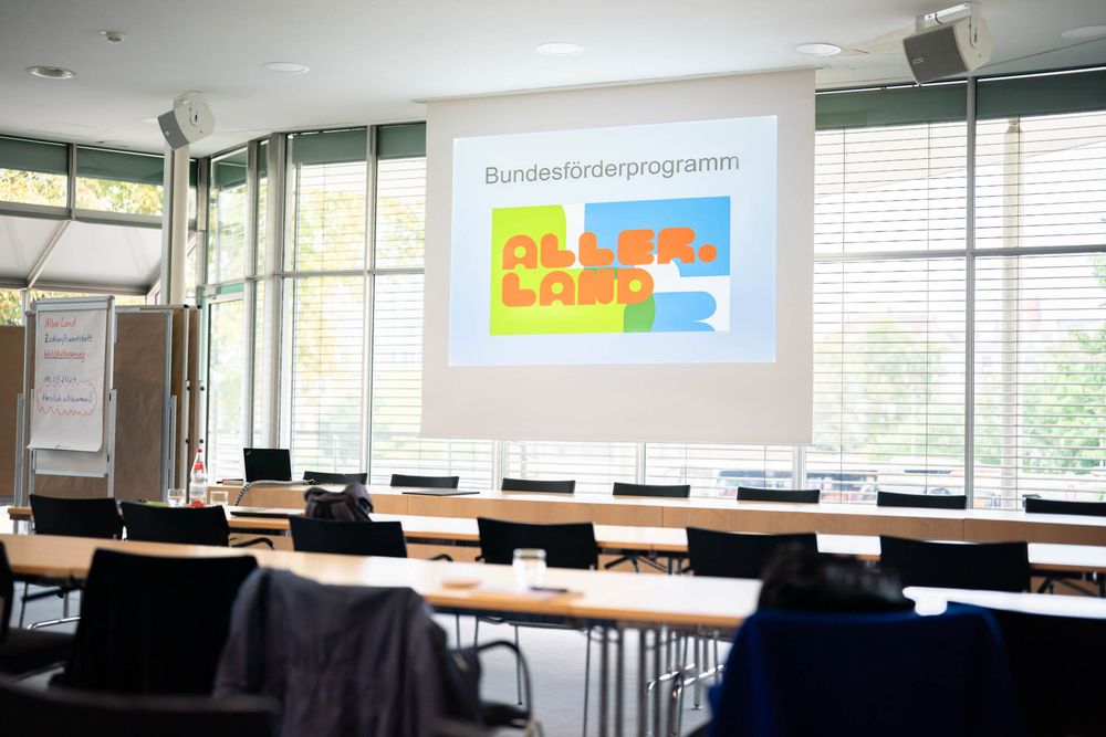 A modern classroom interior with rows of desks, windows, and technology equipment mounted on the walls.