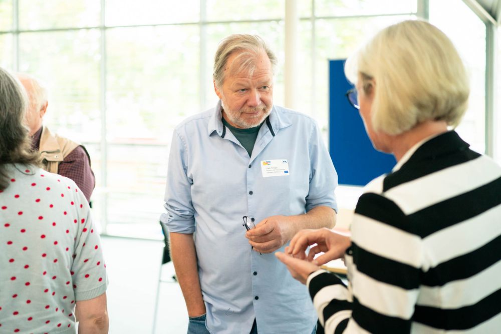 Healthcare worker in blue scrubs provides care to elderly patient in striped sweater during medical consultation.