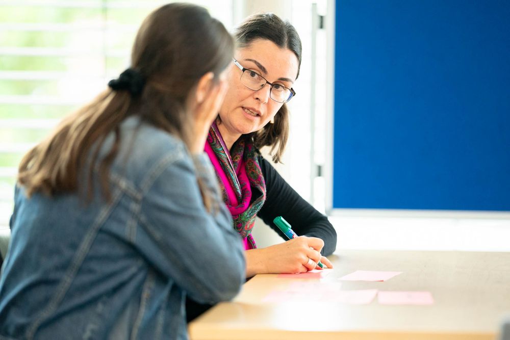 Students work together at tables in a modern classroom with blue walls and bright lighting.