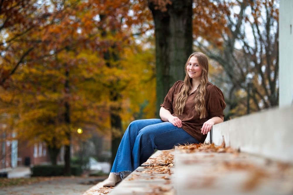 A person sits on concrete steps surrounded by autumn trees with golden leaves falling in the background.