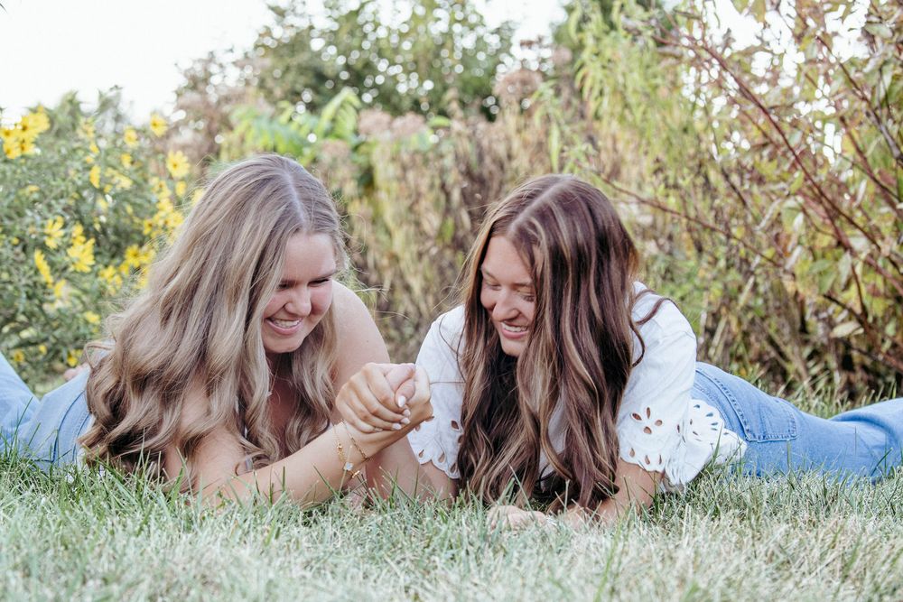 Two people laying in grass having casual conversation among yellow wildflowers during golden hour.