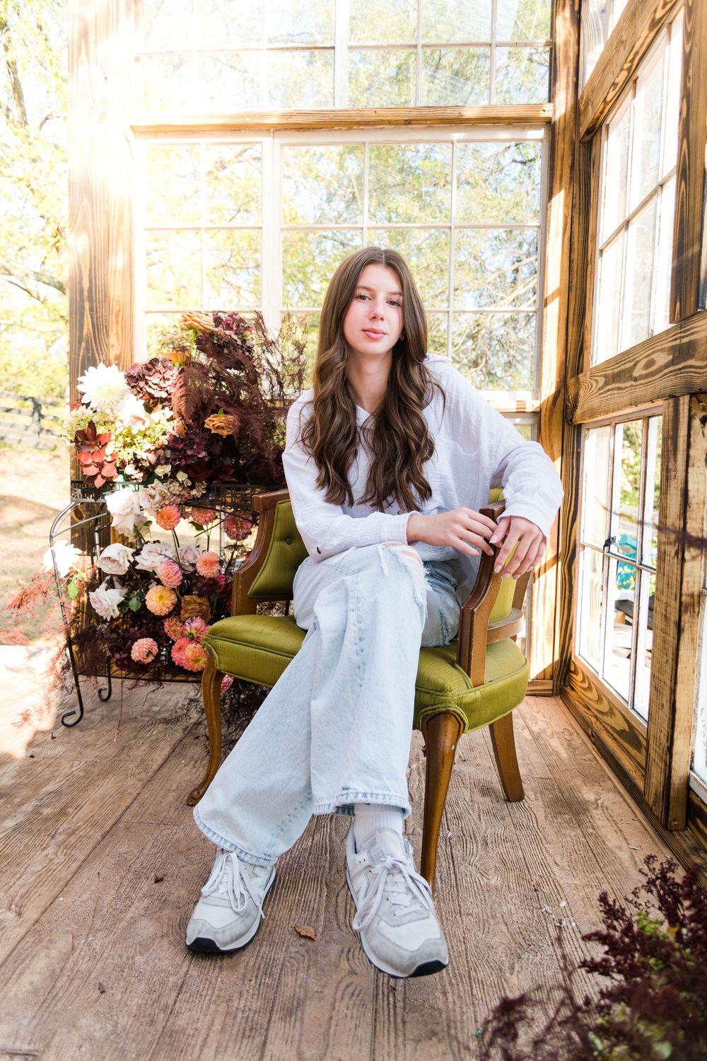 A person in a white dress poses on a rustic wooden porch decorated with floral arrangements and natural lighting.