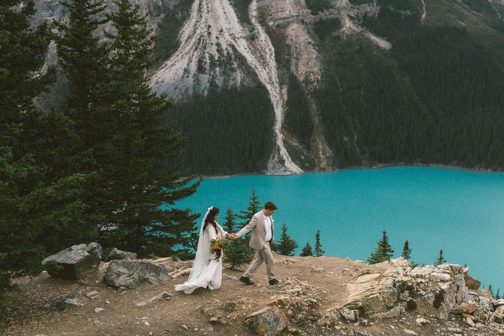 bride and groom walk hand in hand along a rocky outcrop above Peyto Lake in Banff during their elopement