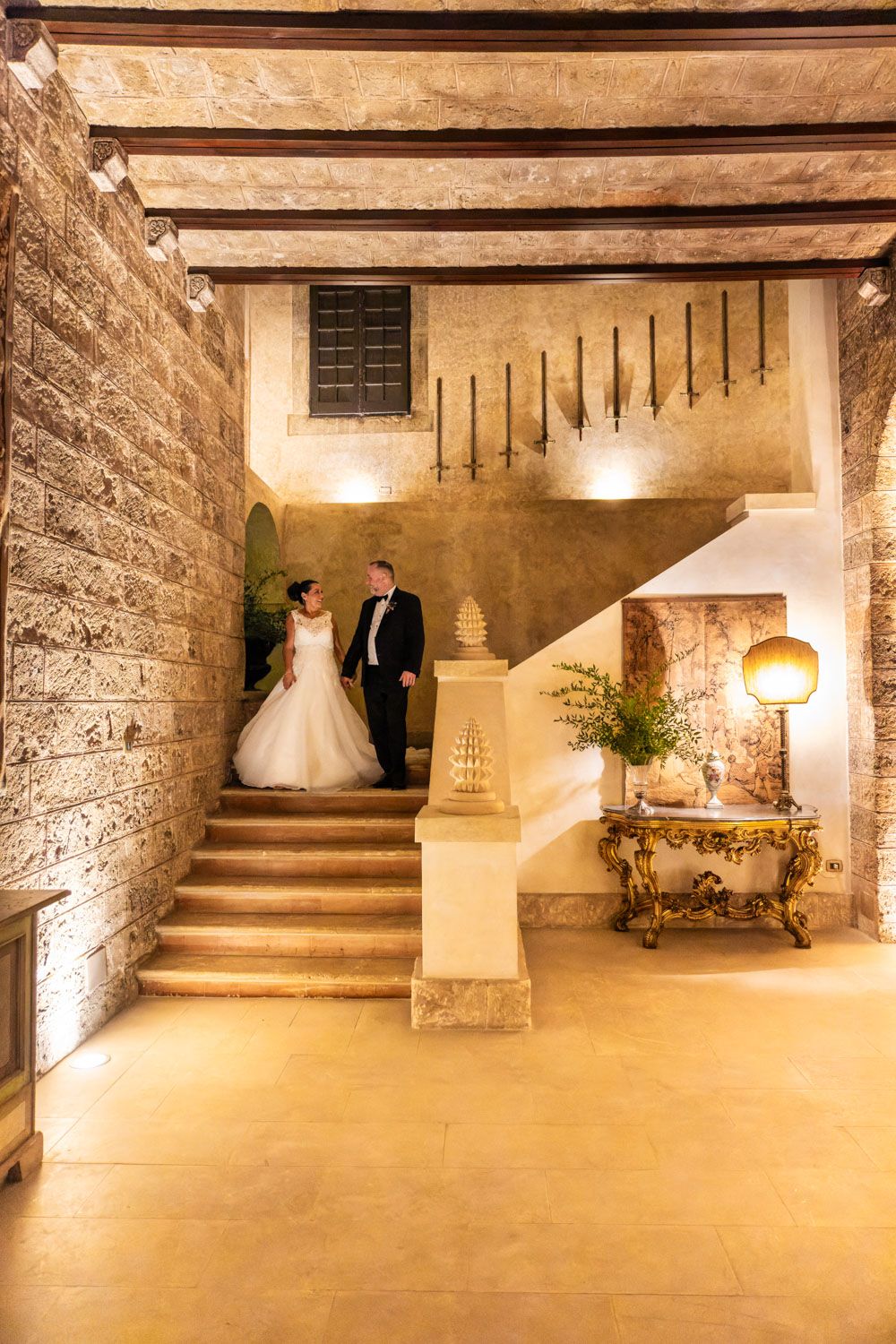 Bride and groom walk down stairs of Italian castle under evening lighting