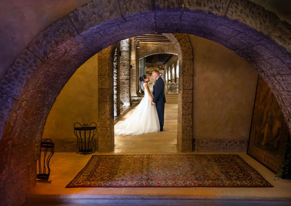 Bride and groom double framed by historic archways at grand Italian castle | Castello Monaci, Puglia