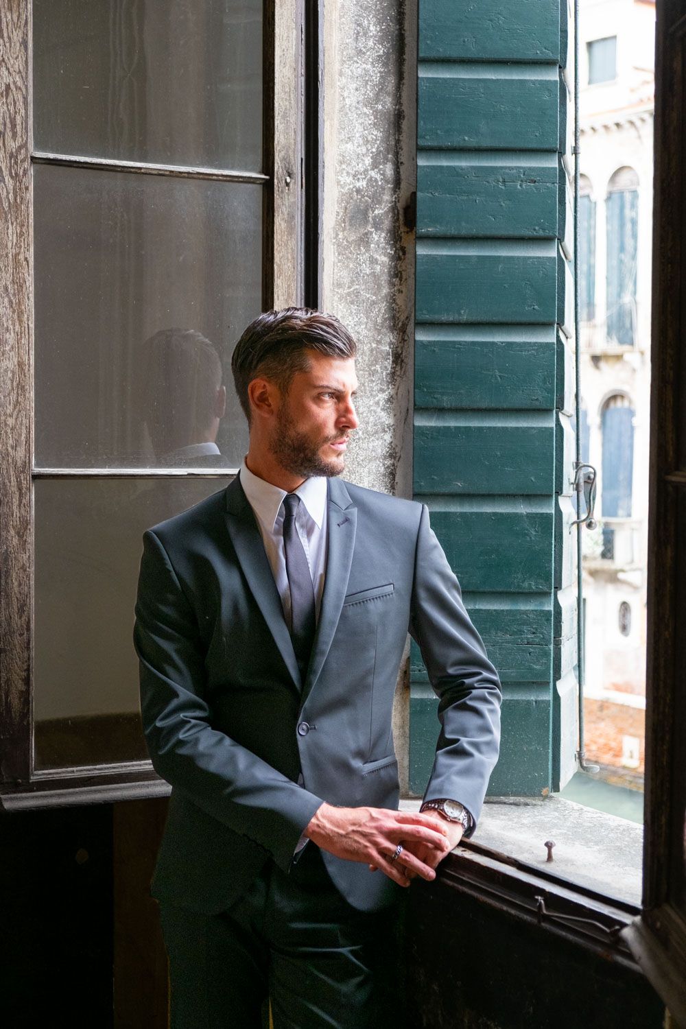 Groom watches out of Venetian palace at the canal
