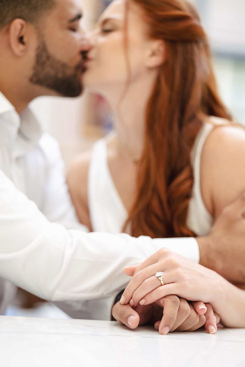 A romantic couple shares an intimate moment while their hands touch gently on a white surface.