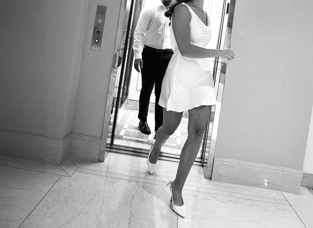 A person in a white dress walking through a bright hotel hallway.