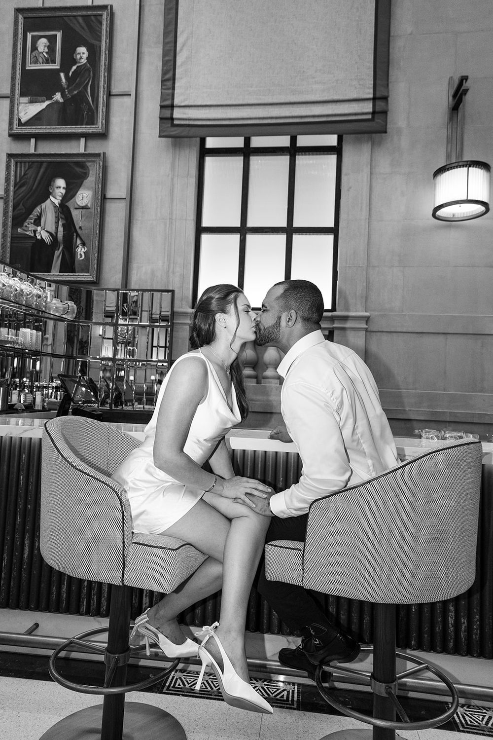 A couple shares a romantic moment at an upscale hotel bar with vintage artwork on the walls.