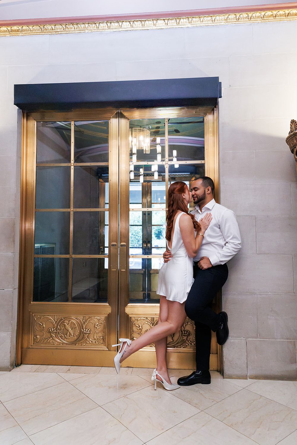 A couple embraces by ornate gold elevator doors in a luxury hotel.