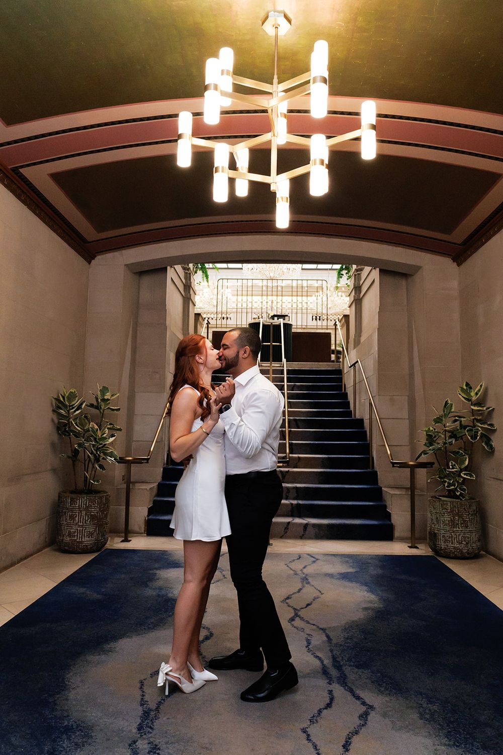 A couple shares a romantic moment in a dimly lit hallway with modern lighting fixtures and potted plants.
