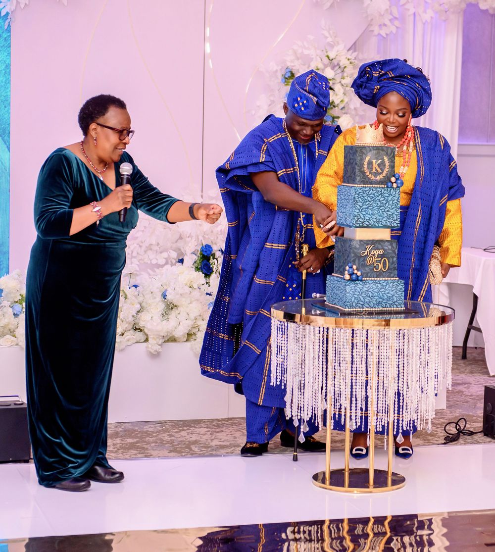 Wedding reception table decorated with elegant blue and gold cake and floral arrangements at an indoor venue.