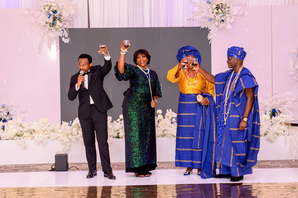 A group of people in formal attire celebrate at a wedding reception with traditional African and Western dress styles.