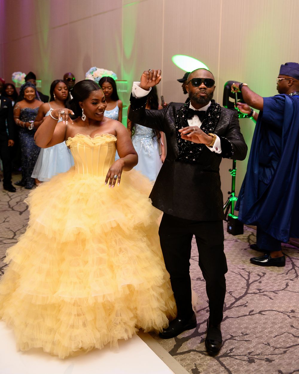 A couple dances together at a celebration, with the bride wearing a voluminous yellow tulle ballgown.