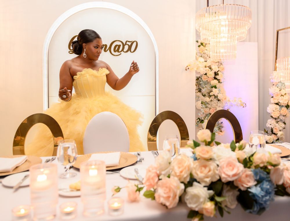 A person in a yellow gown dances at an elegant reception with floral centerpieces and arched decor.