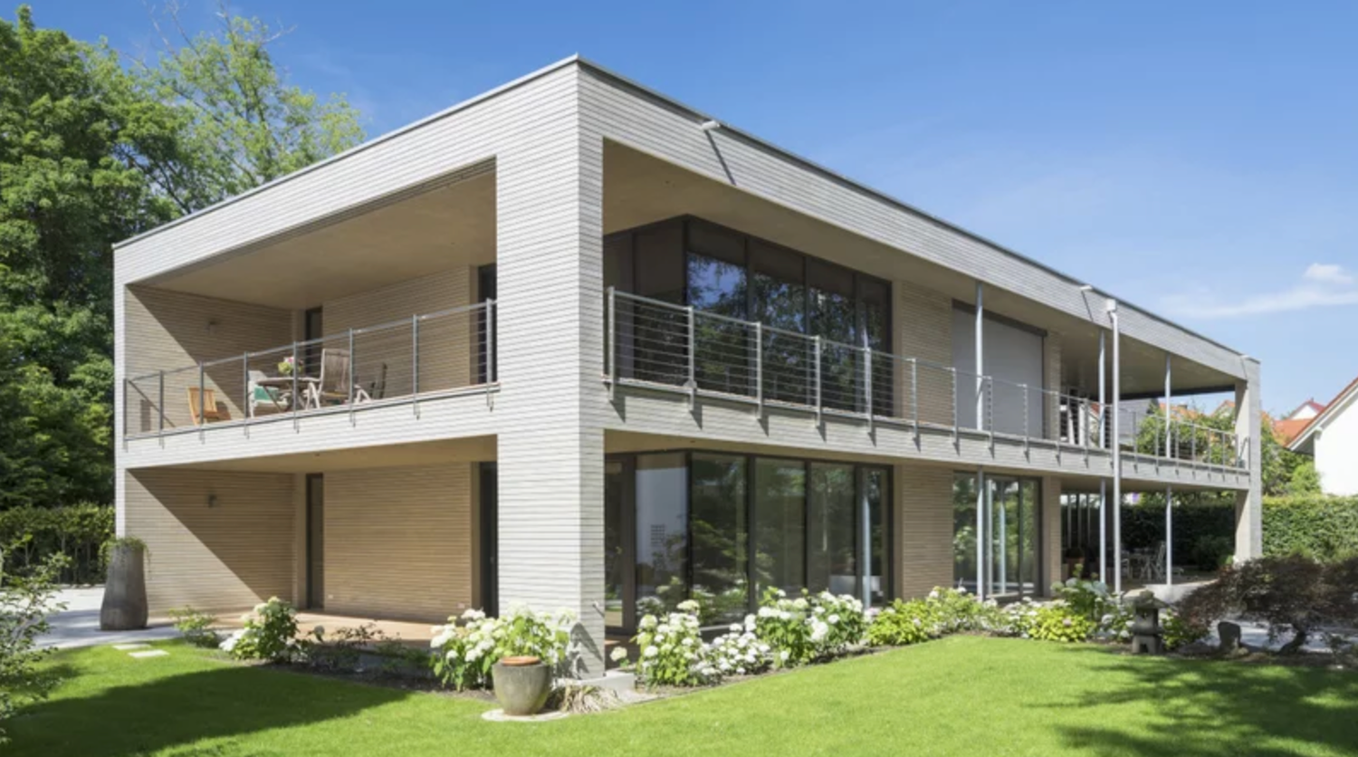 Contemporary white building with glass windows and sloped design nestled on a grassy hillside.