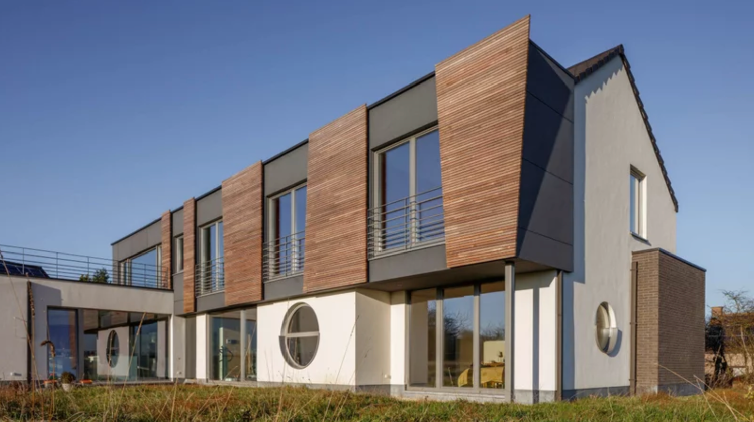 Modern luxury homes with wood accents and large windows form a panoramic view against a bright blue sky.