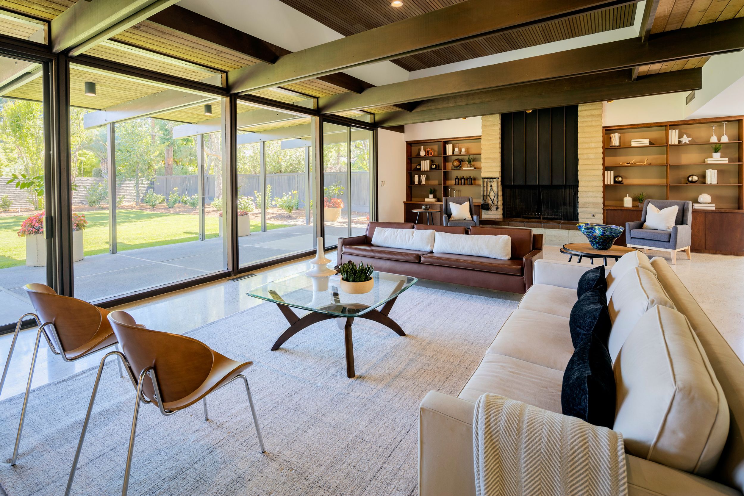 Modern open-concept living room features floor-to-ceiling windows, wood ceiling beams, and contemporary furnishings.