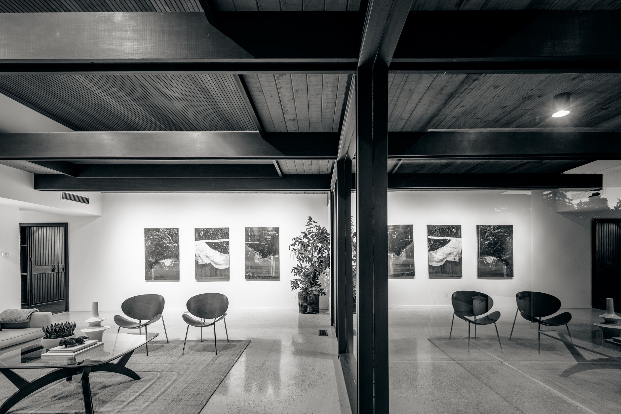 A sleek modern interior with black chairs and exposed ceiling beams in a minimalist white space.