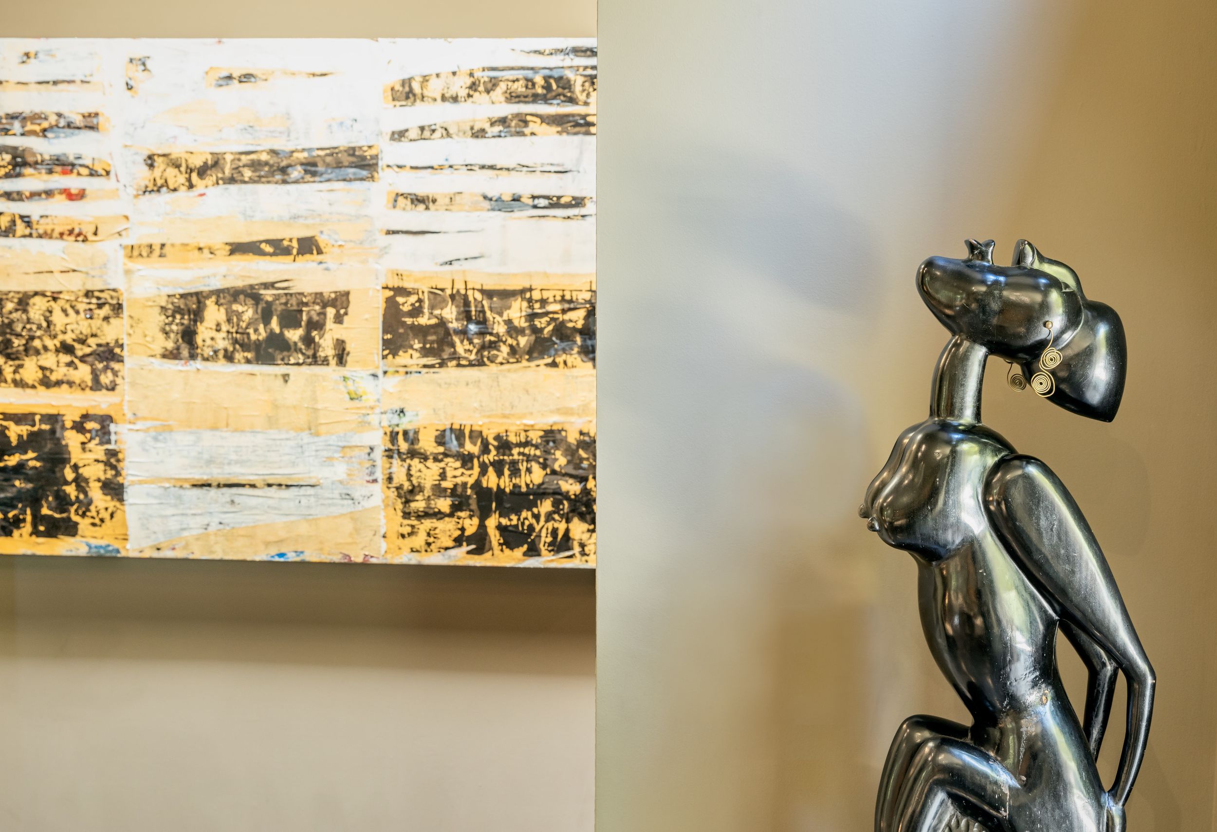 Bronze sculpture of a nude figure in contemplative pose against a textured beige wall with artistic lighting.