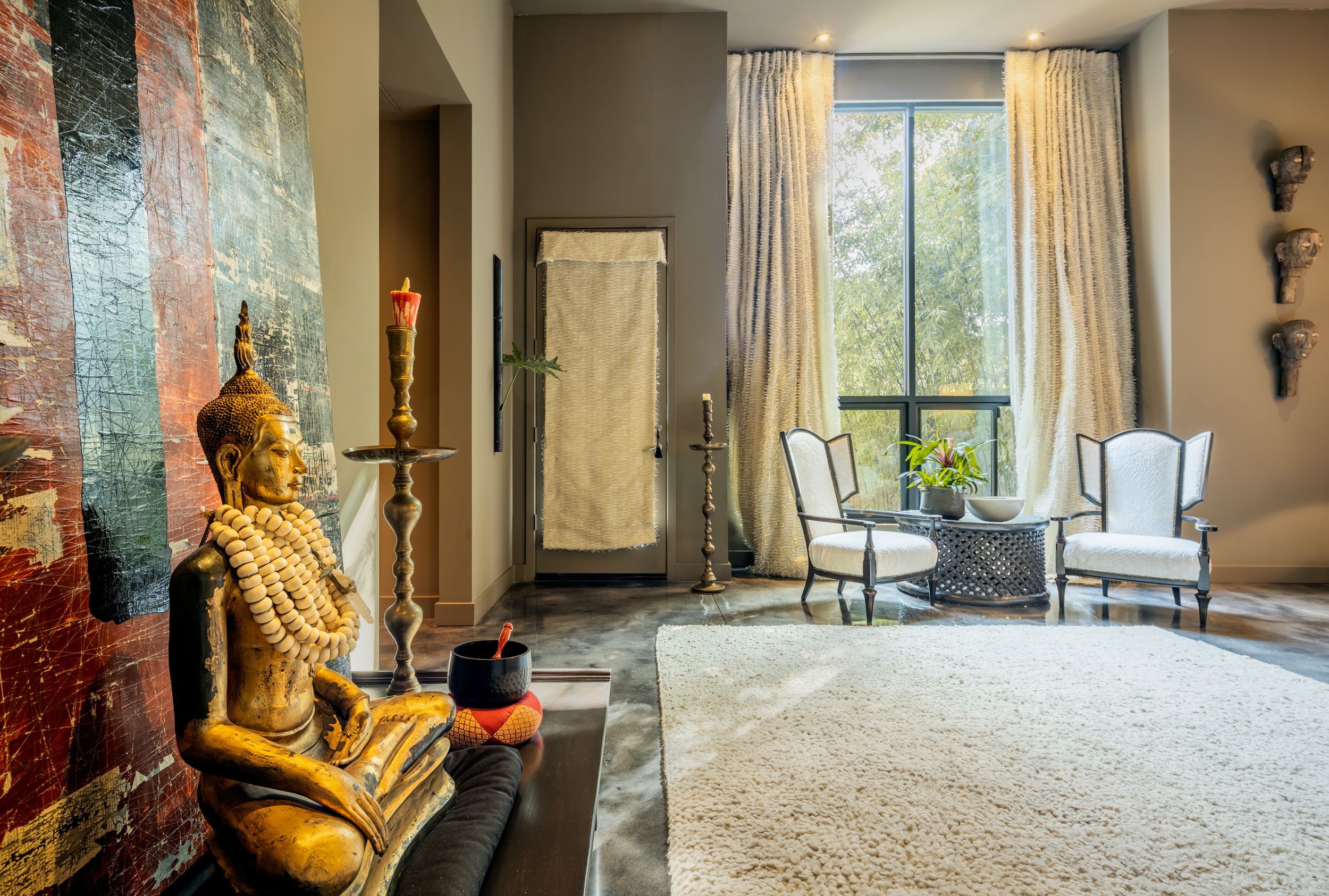 Elegant living space with floor-to-ceiling windows, neutral decor, and plush seating arranged around a stone fireplace.