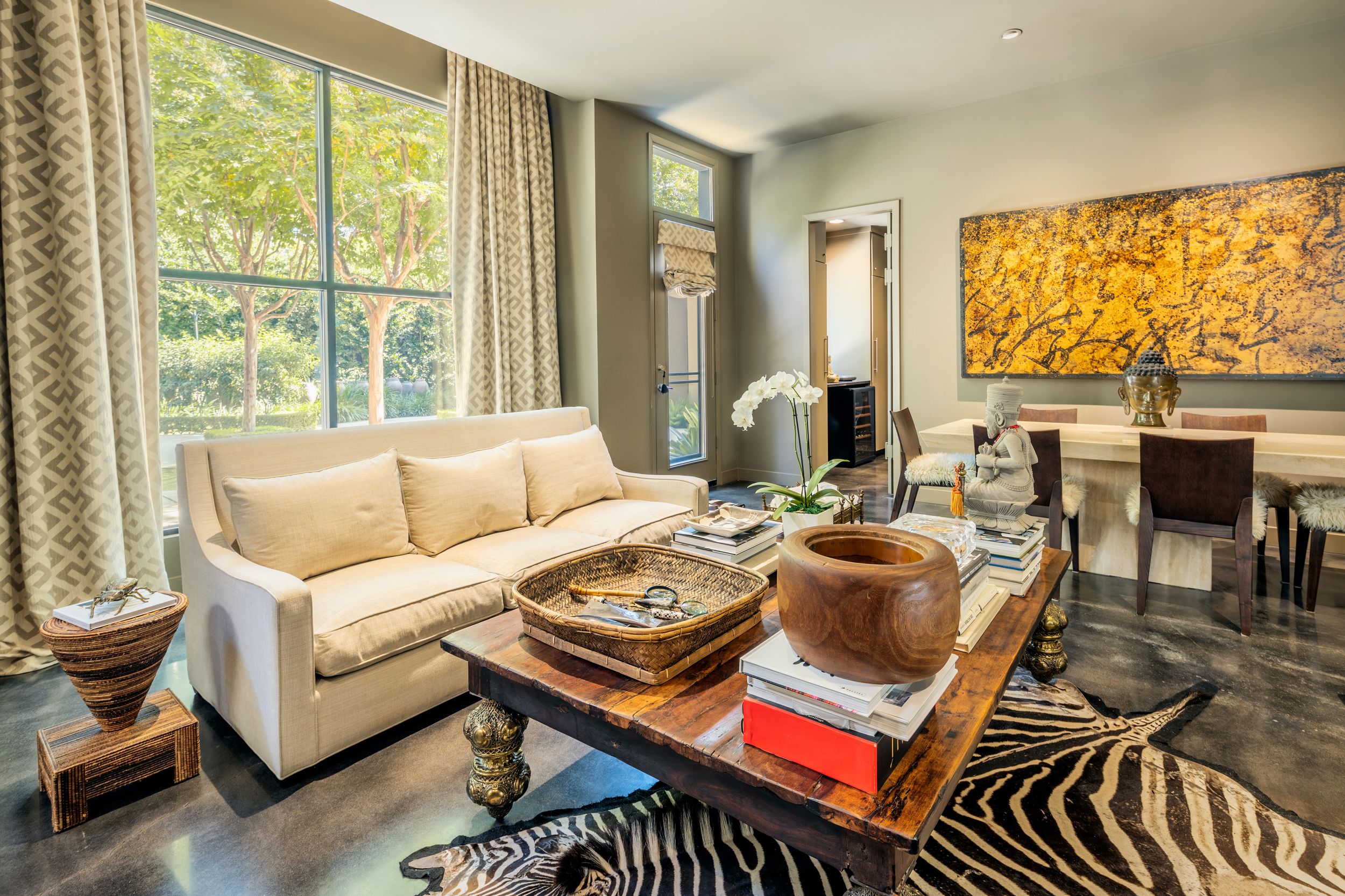 Modern open concept living room features zebra print rug, beige sofas, and large windows overlooking natural scenery.