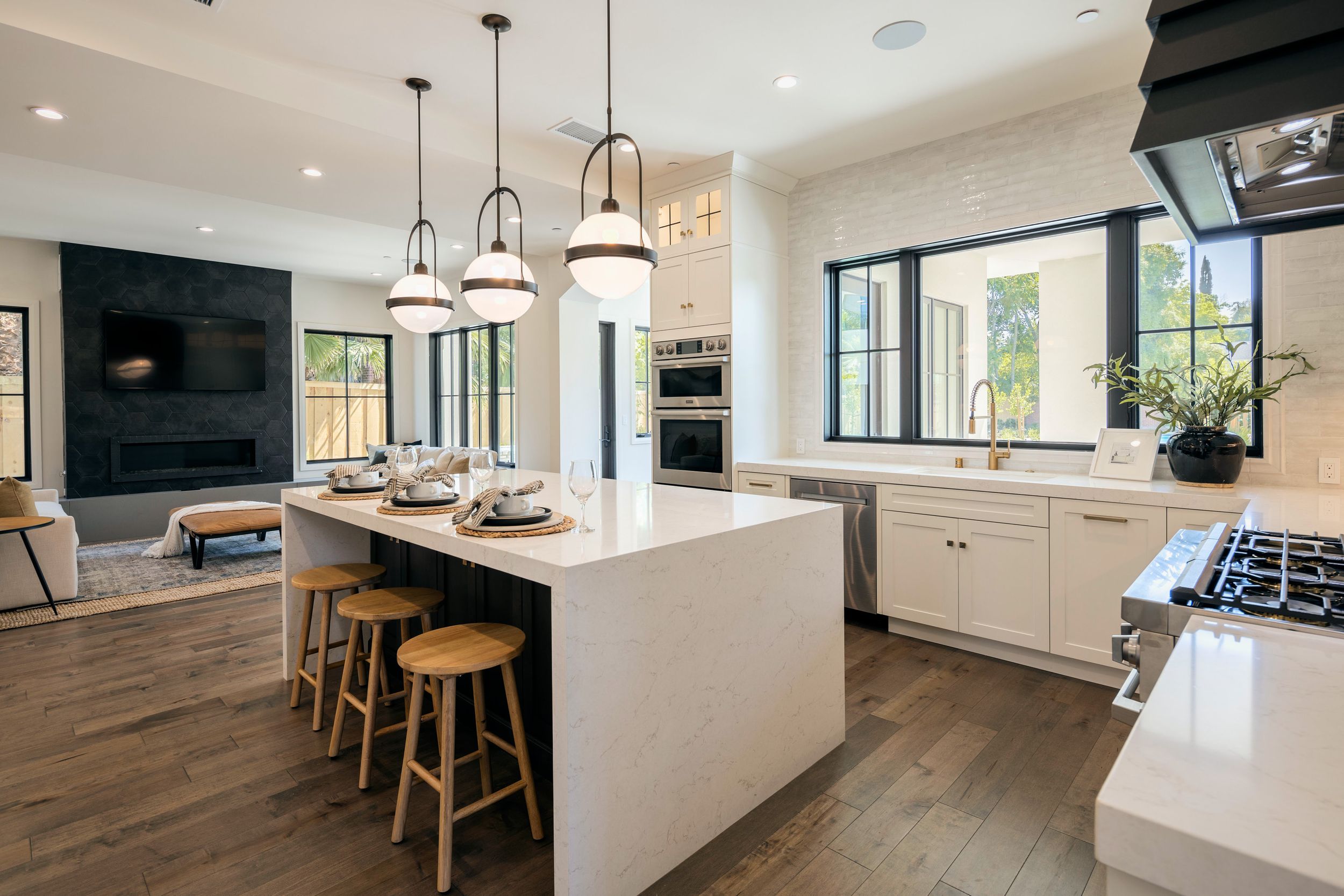 Modern open concept kitchen and living area features white cabinetry, pendant lighting, and hardwood floors in neutral tones.