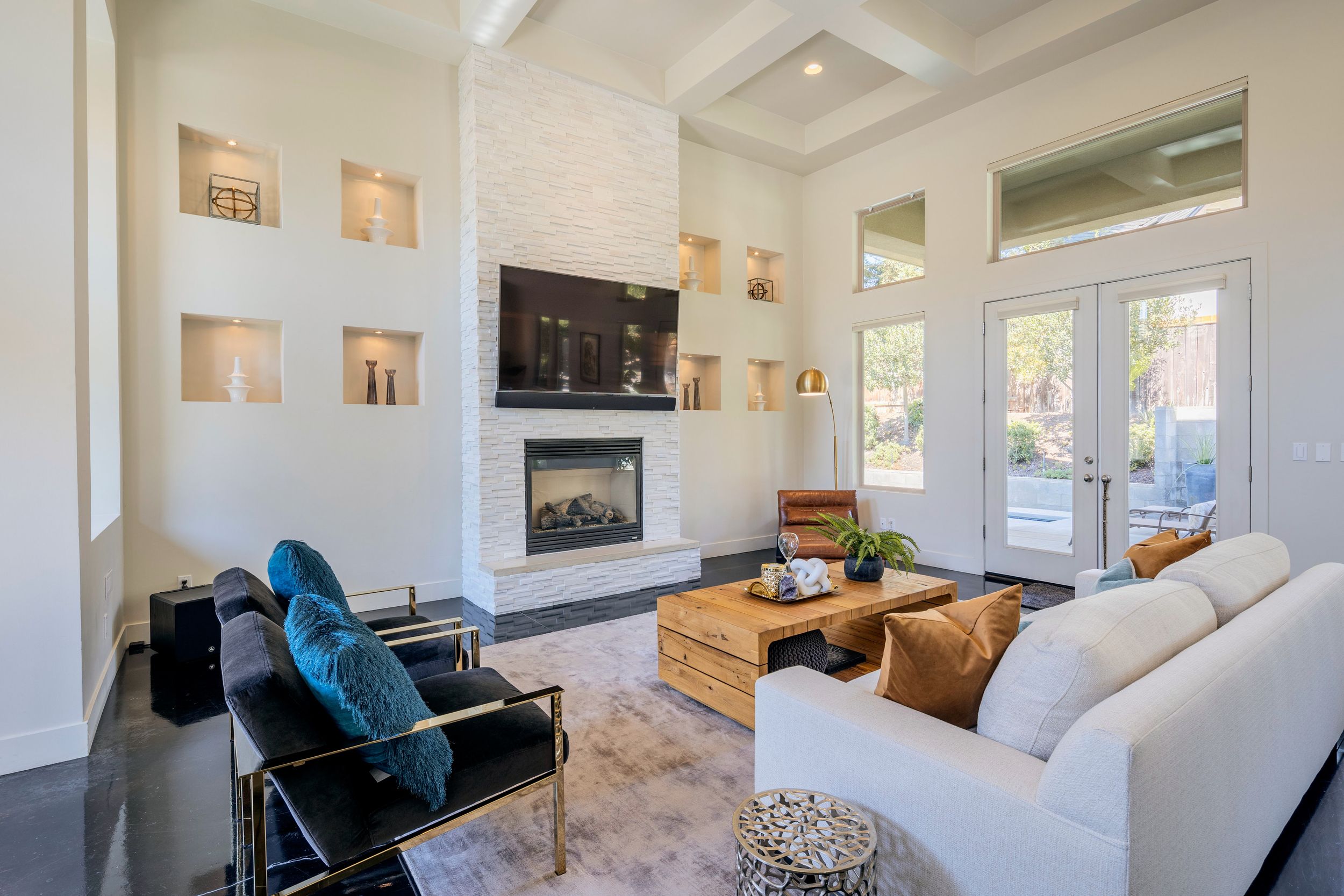 Modern white living room features vaulted ceilings, built-in shelves, and turquoise accent chairs around a sleek fireplace.