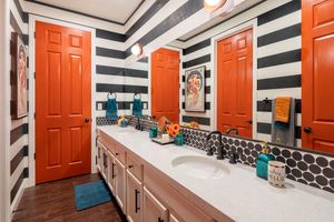 Modern bathroom interior with bold orange doors and black and white striped walls creating a dramatic geometric pattern.