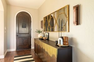 A long hallway with cream walls features dark wooden doors, gold-framed mirrors, and warm lighting casting shadows.