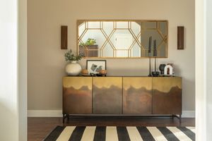 Modern entryway featuring a gold mountain-motif credenza, geometric mirror, and black and white striped rug.