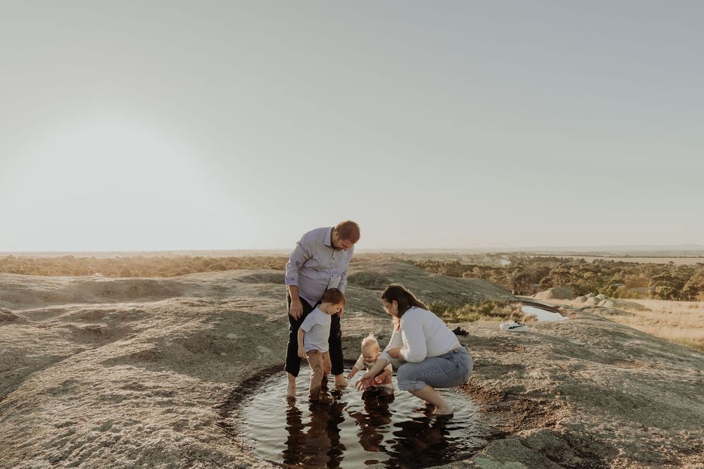 Family of three playing in a shallow rock pool in an arid outdoor landscape.