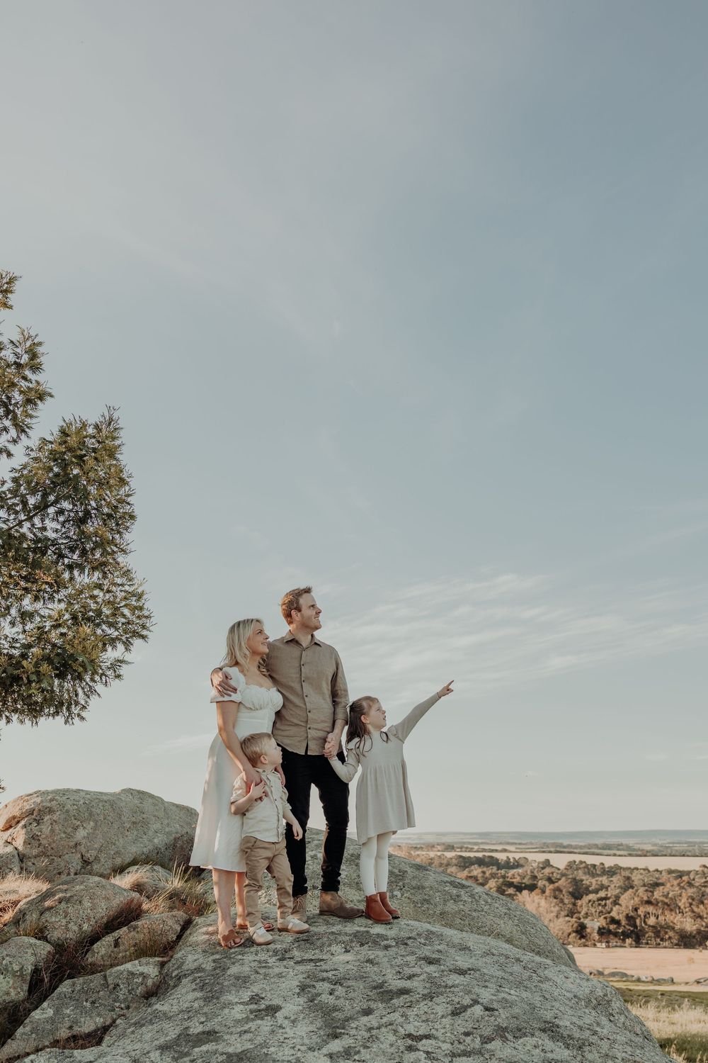 Family of four standing on rocky summit, young girl pointing at the horizon at sunset.