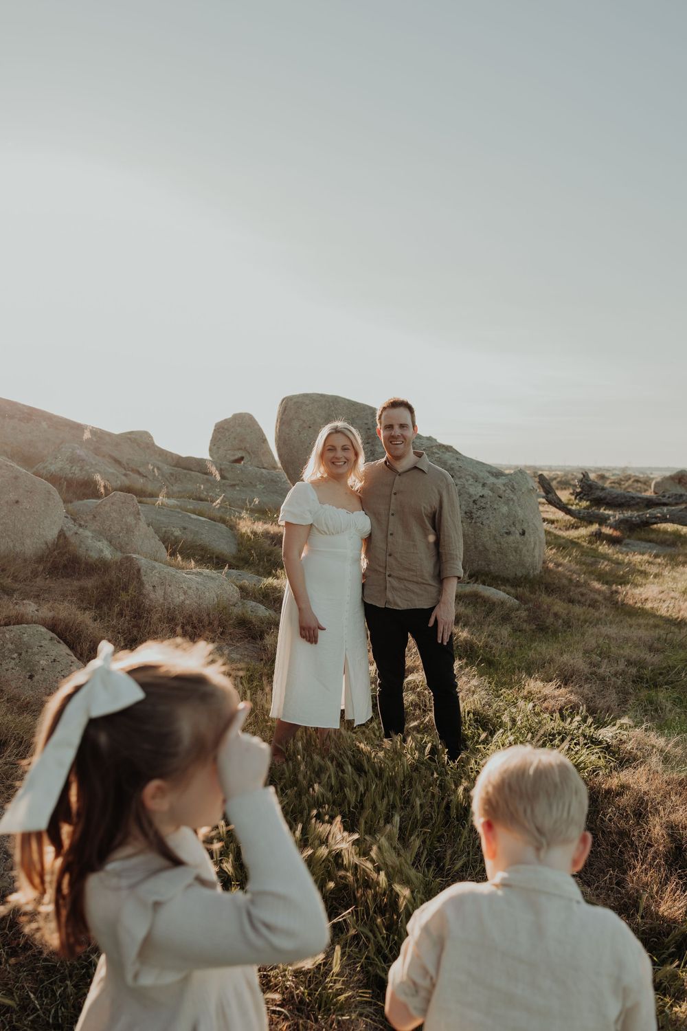 Smiling couple standing among granite boulders while two children play in the foreground.