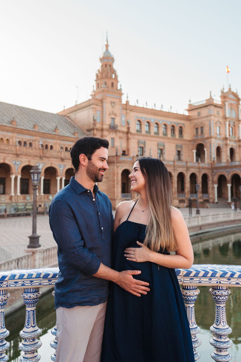 A couple embraces and smiles at each other on a bridge at Plaza de España in Seville, Spain.