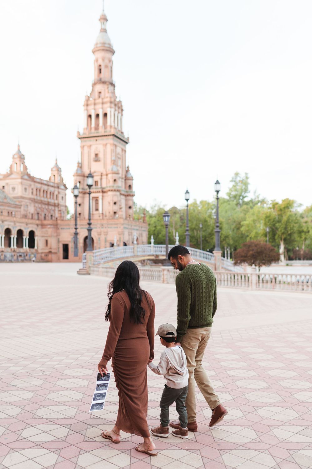 A family walks together across the expansive plaza with Spanish baroque towers in the background.
