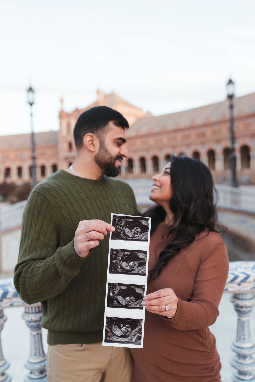 A couple shares a special moment while holding ultrasound photos at Plaza de España.