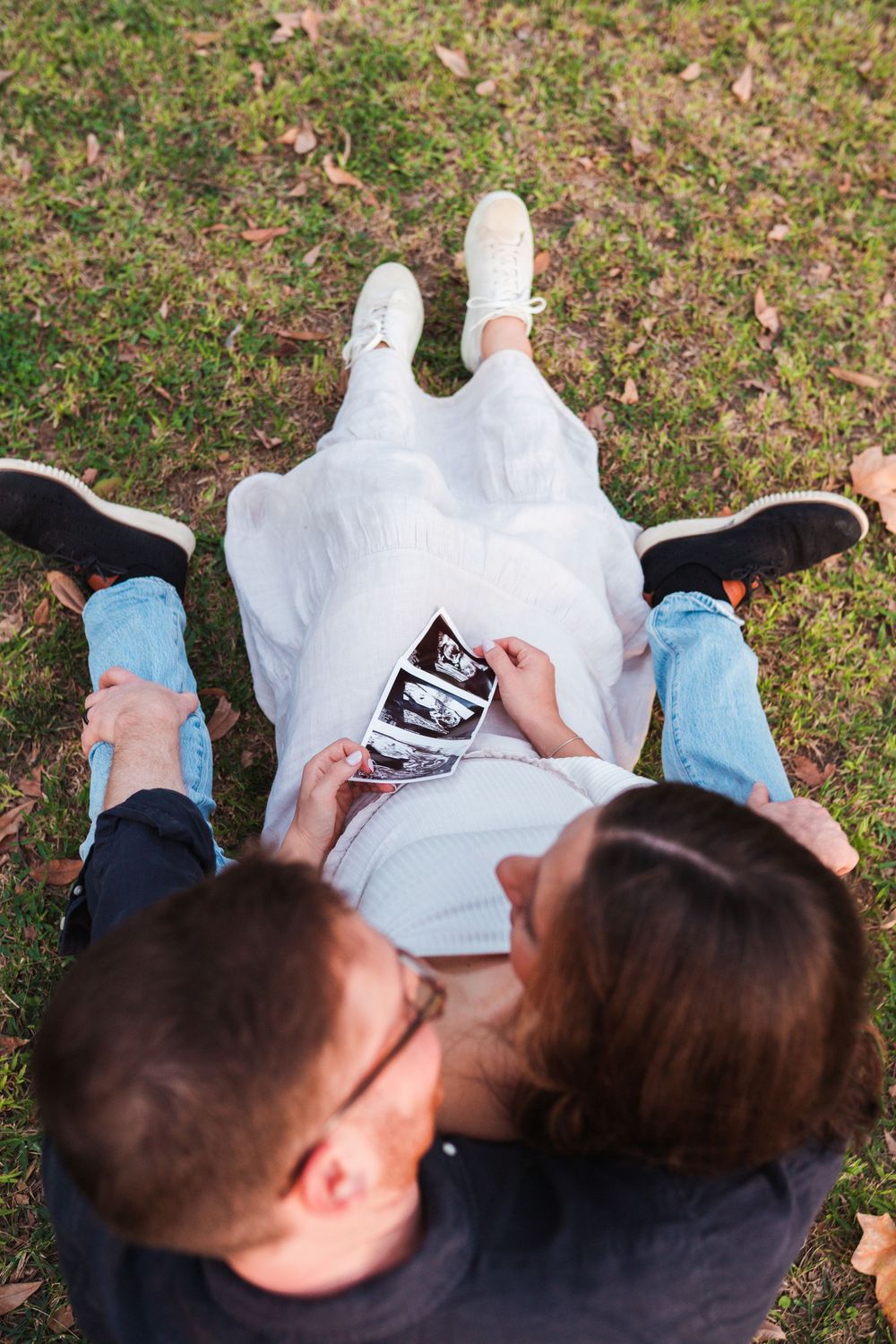 Couple looking at ultrasound photos while sitting together on grass.