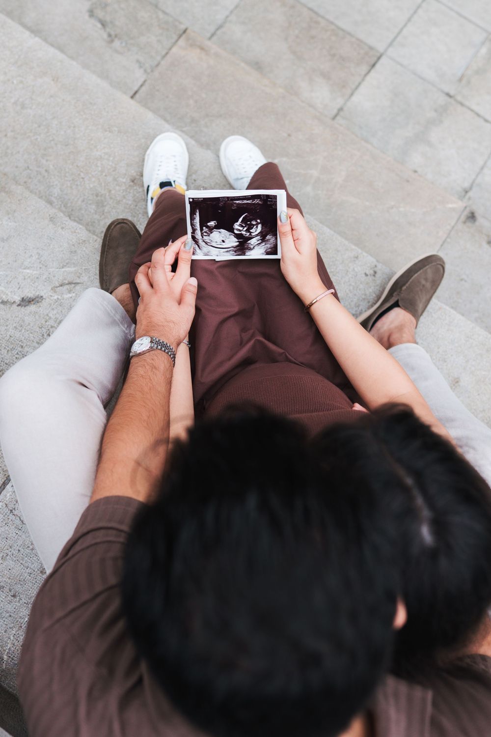 Overhead view of couple looking at ultrasound photo while sitting on stone floor.