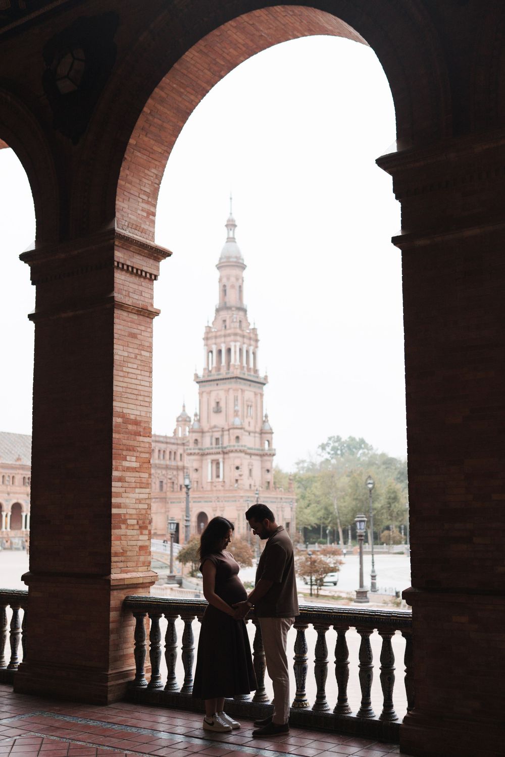 Silhouettes under brick archways with Spanish plaza and tower in background.