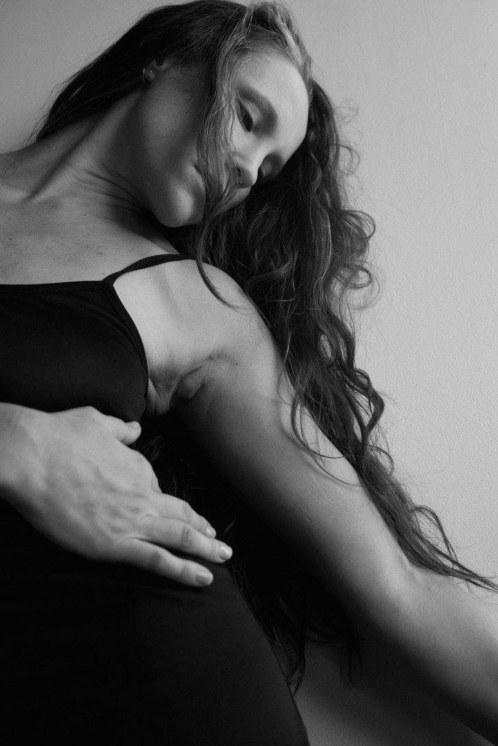 Black and white close-up of a woman with long wavy hair in a black dress posing gracefully.
