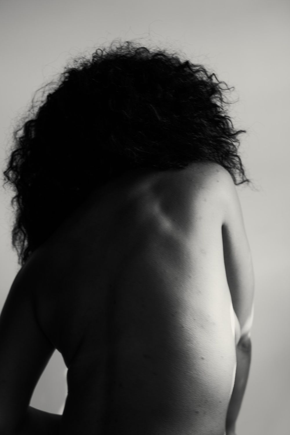 Black and white rear view of a nude woman with curly hair against a light background.