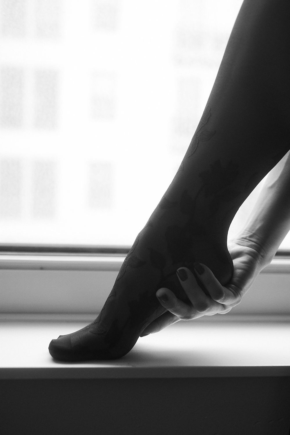 Black and white close-up of hand holding foot on windowsill.