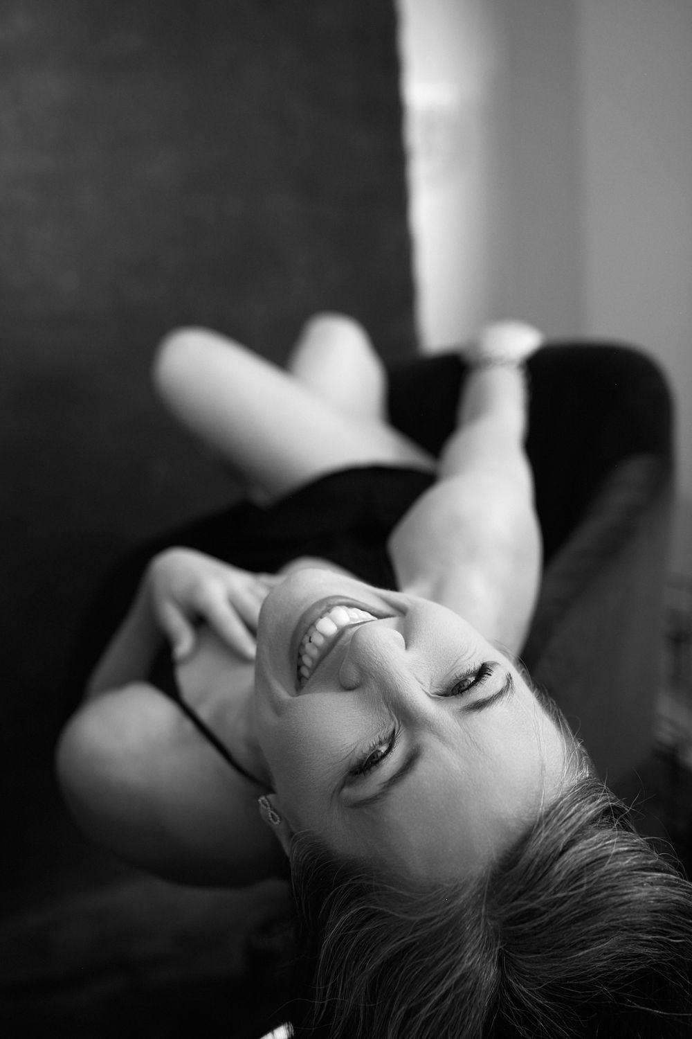 Black and white photo of a laughing woman lying back on a sofa, looking carefree and joyful.