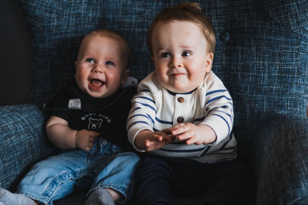 Baby in striped shirt smiling and playing during indoor family photoshoot.