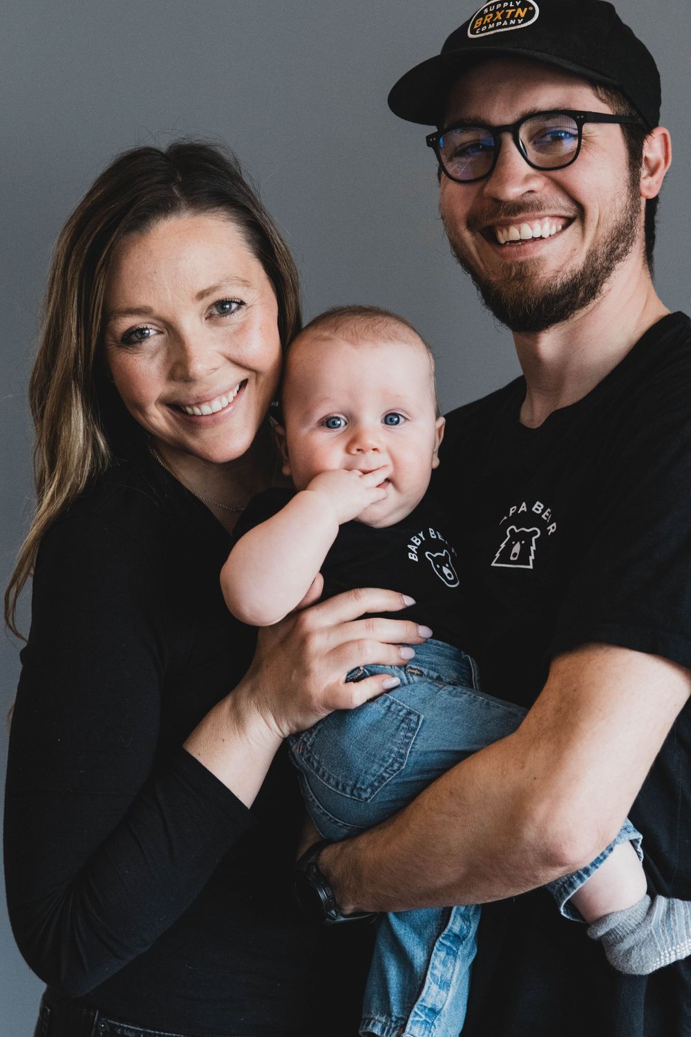 Series of candid family moments with baby wearing denim in studio against grey backdrop.