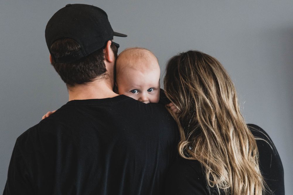 Family photo session showing tender moments between parents and baby against grey backdrop.