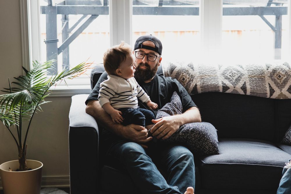Family relaxing together with their dog on a gray couch near bright windows.
